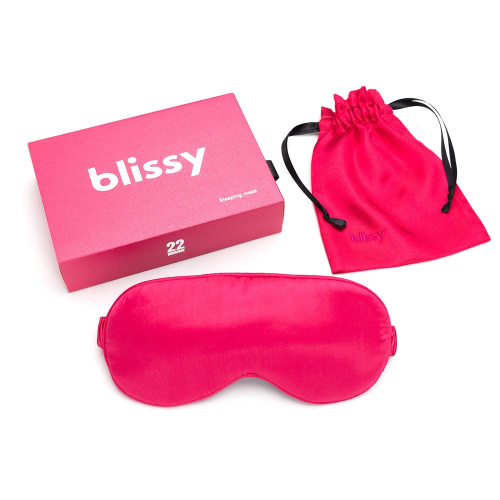 Hot pink silk sleep mask with adjustable elastic strap, matching drawstring pouch, and branded pink packaging box