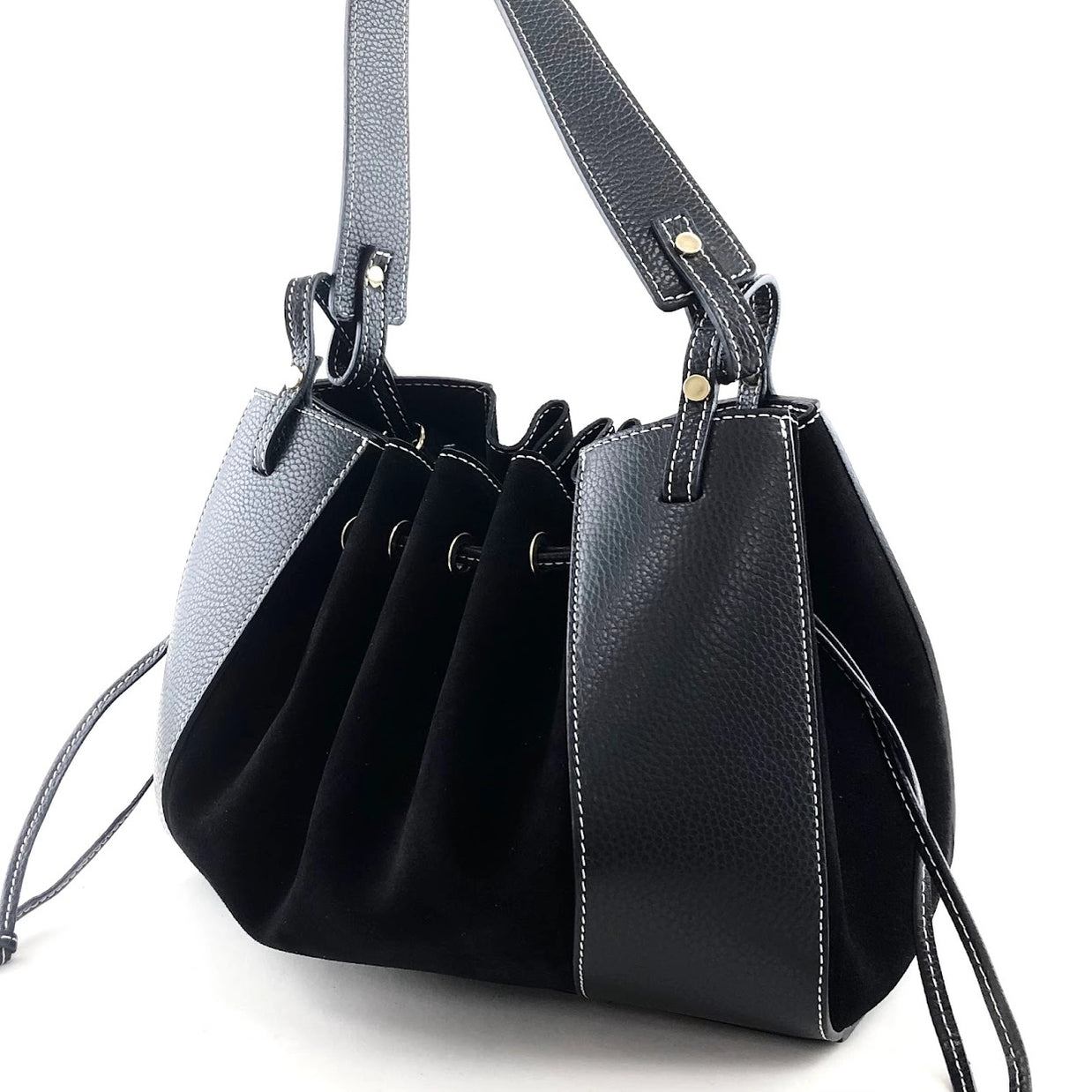 Black pebbled leather bucket bag with ruched suede panel, contrast white stitching, and dual shoulder straps with gold hardware.