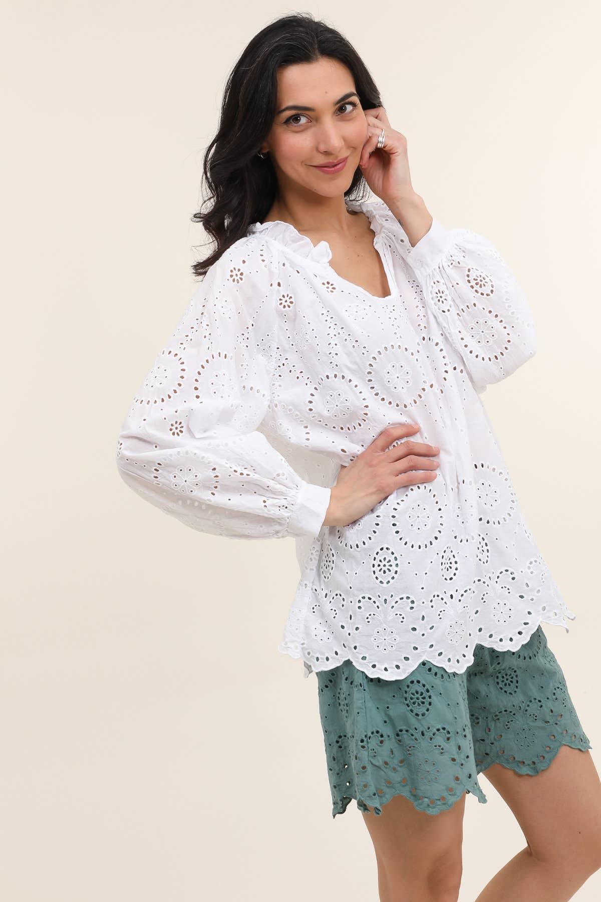 White cotton eyelet lace blouse with puff sleeves and scalloped hem paired with sage green eyelet shorts on beige background
