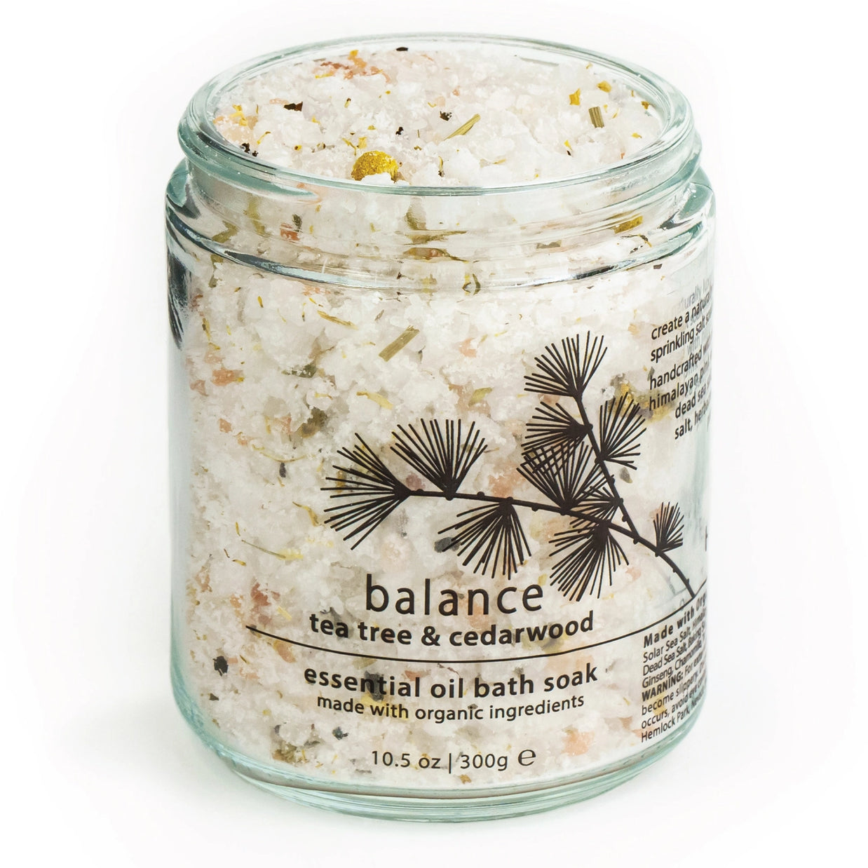 Clear glass jar filled with white bath salts mixed with dried botanical herbs and golden flecks, cedarwood branch label