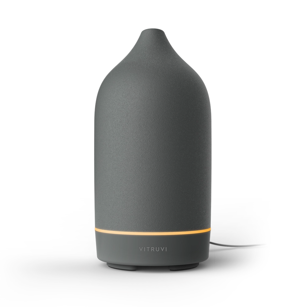 Charcoal gray ceramic essential oil diffuser with dome-shaped top, gold accent band, and Vitruvi branding on matte finish base