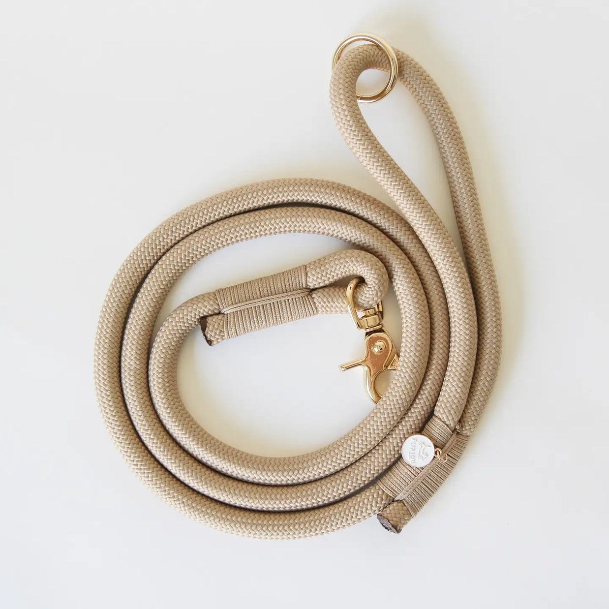 Beige braided rope dog leash with rose gold lobster clasp and O-ring, coiled on white surface with matching collar