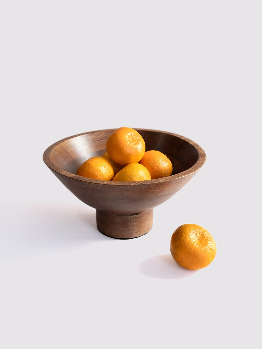Turned walnut wood pedestal fruit bowl with smooth curved sides holding five bright orange citrus fruits on white surface