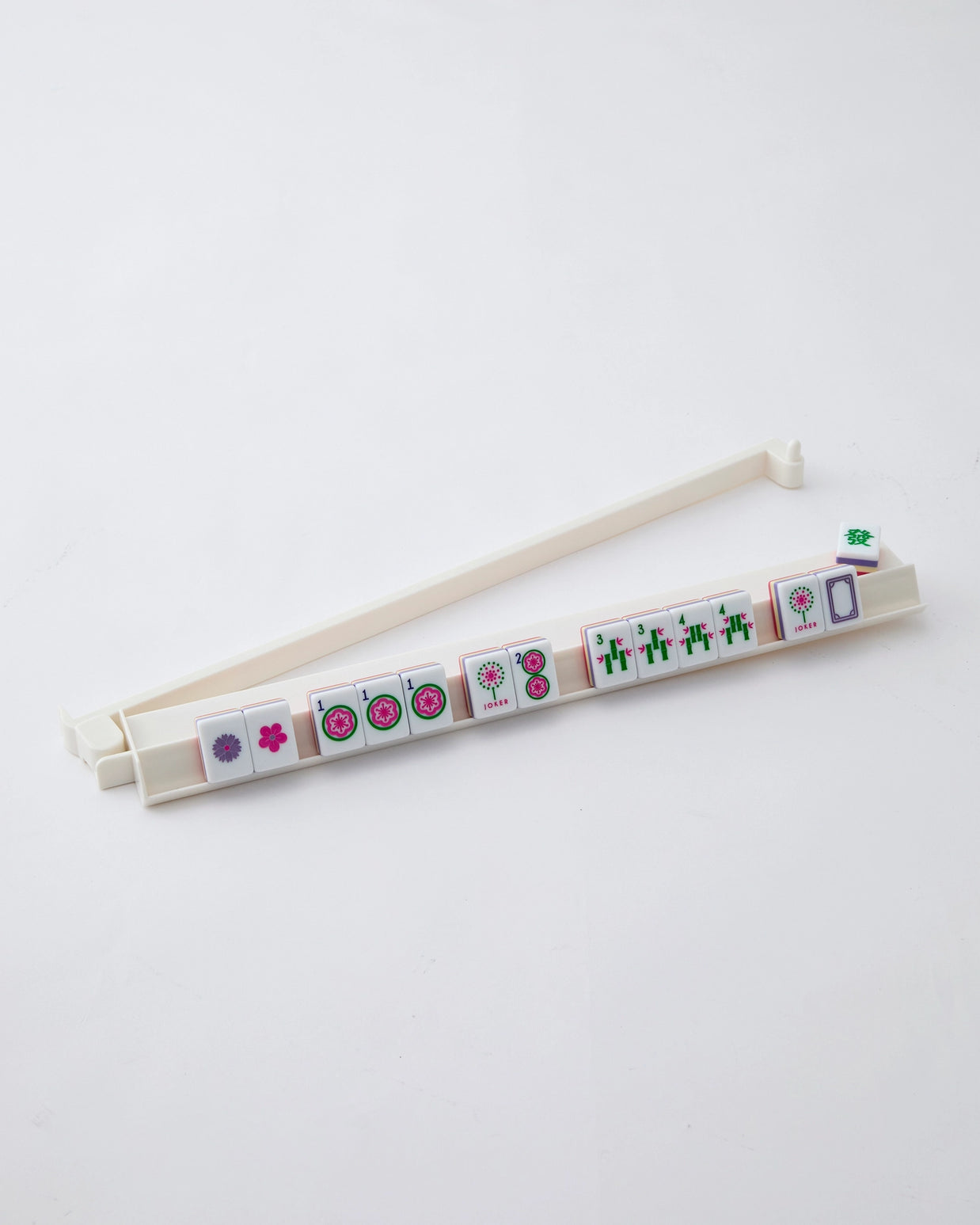 Cream plastic mahjong tile rack holding decorated tiles with pink flowers, green bamboo, and circle patterns on white background
