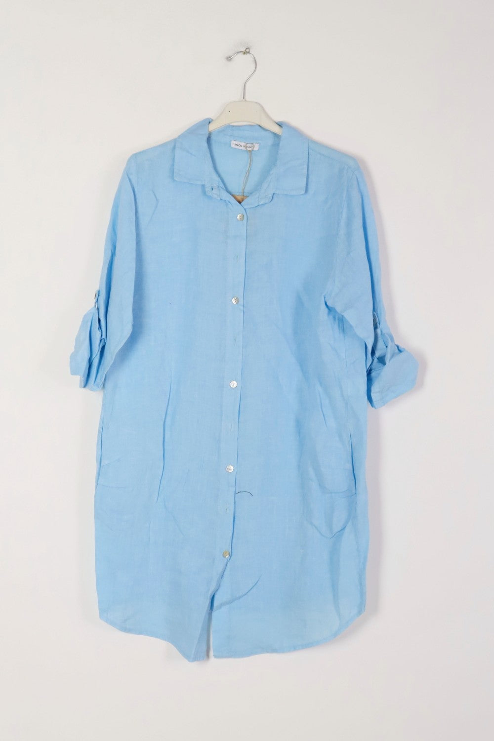 Sky blue linen shirt dress with white button front, rolled cuffed sleeves, patch pockets, and collar on white hanger