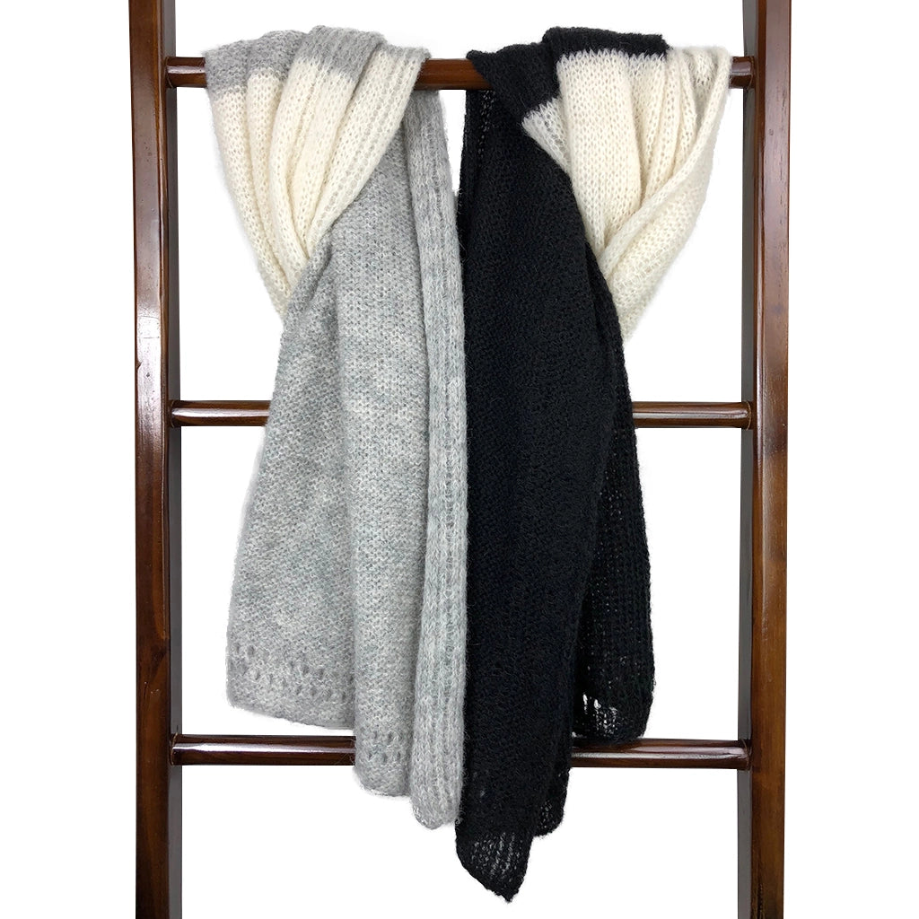 Chunky hand-knit throw blanket in cream, gray, and black panels draped over wooden ladder rack with textured stitches