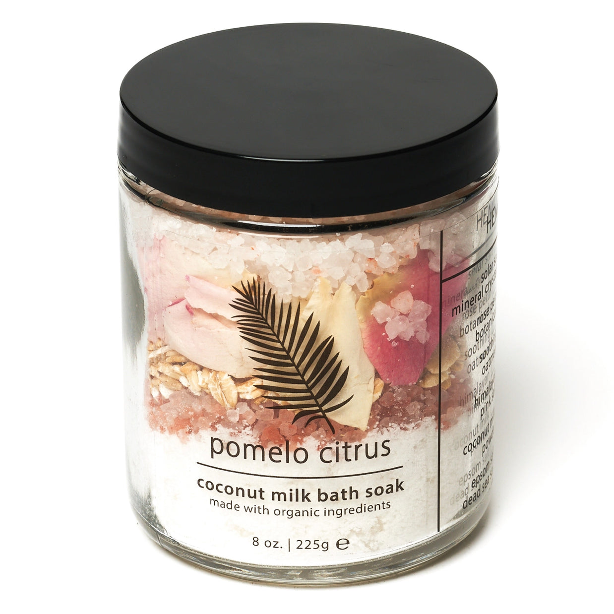 Clear glass jar with black lid containing layered pink and white bath salts, dried flowers, and palm leaf decoration