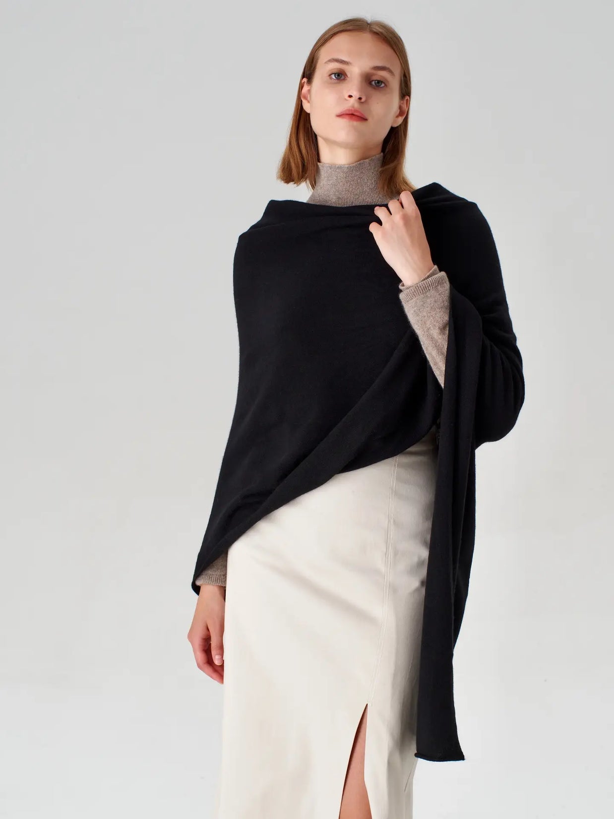 Black cashmere wrap draped asymmetrically over gray turtleneck and cream skirt, featuring long sleeves and flowing silhouette