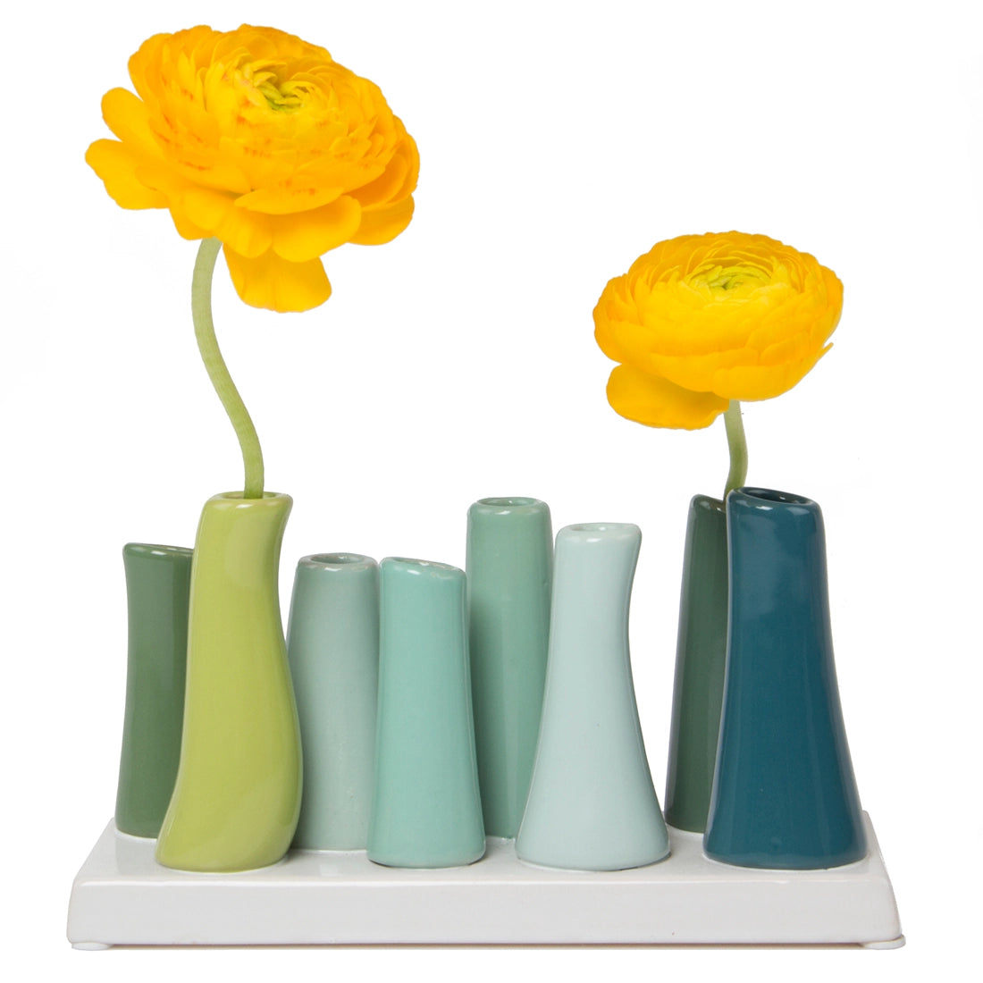 Ceramic bud vase set with eight tapered tubes in gradient blue and green glazes holding yellow ranunculus flowers