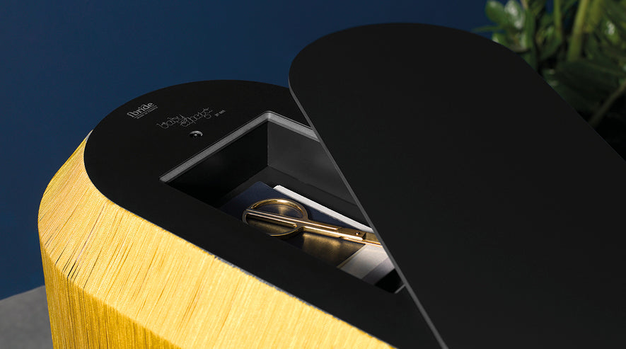 Modern turntable with matte black top, yellow wood grain veneer sides, and bronze-toned tonearm on navy background