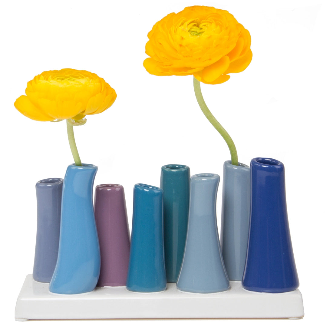 Multi-tube ceramic bud vase in gradient blues and purples on white tray with two yellow ranunculus flowers