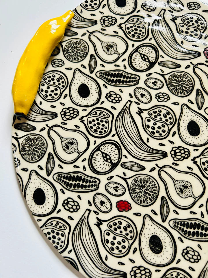 Ceramic serving platter with black and cream hand-drawn fruit pattern including bananas, avocados, pomegranates, and citrus slices