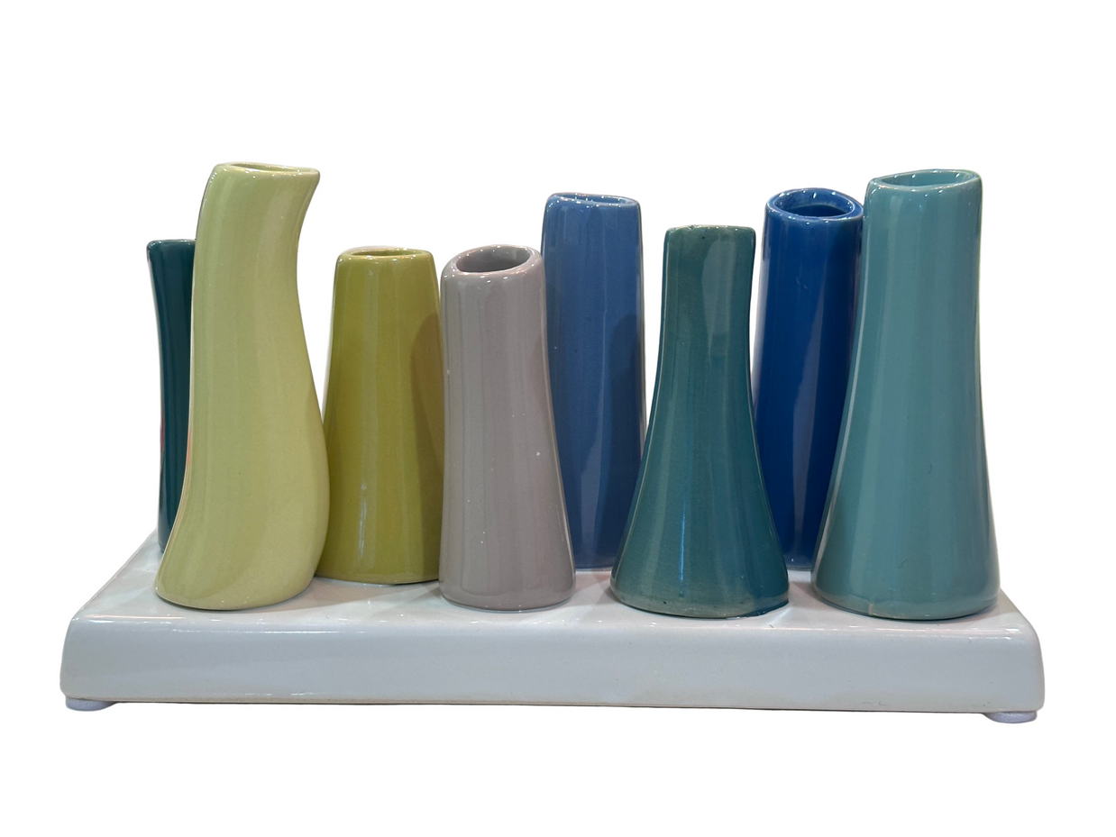 Ceramic bud vase set with nine tubular vessels in varied heights glazed in teal, sage, olive, gray, and blue on white tray