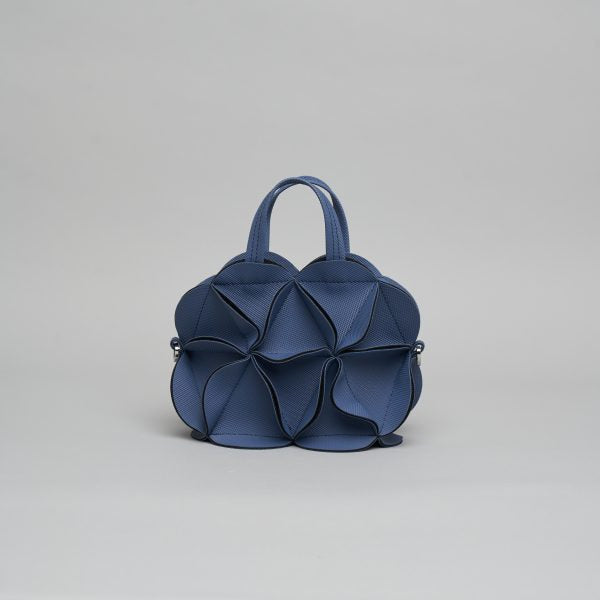 Navy blue leather handbag with sculptural petal design forming a flower-like structure, dual top handles and crossbody strap