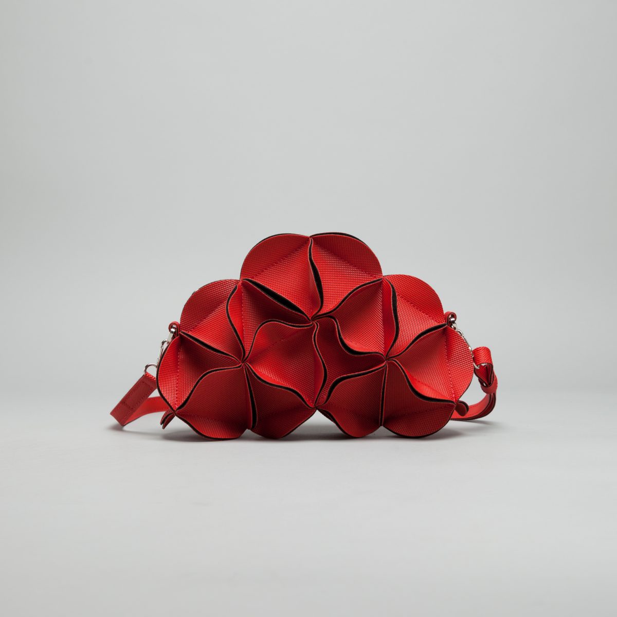 Sculptural red crossbody bag shaped like overlapping flower petals with textured surface and burgundy piped edges