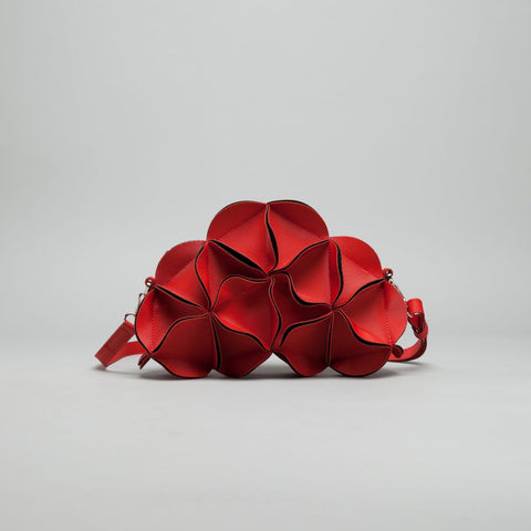 Sculptural red crossbody bag shaped like overlapping flower petals with textured surface and burgundy piped edges
