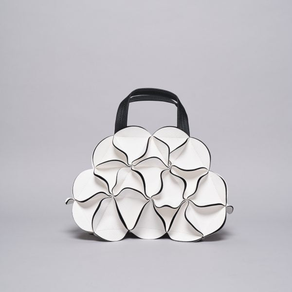 White sculptural handbag with seven circular petal-shaped compartments outlined in black piping and black top handle