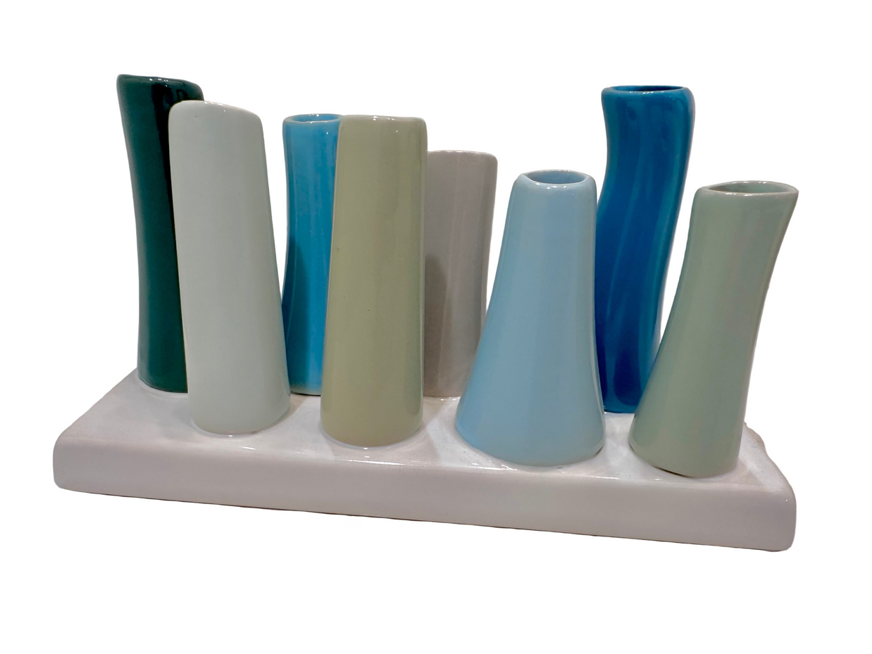 Modern ceramic bud vase set with nine cylindrical tubes in teal, cream, blue and gray glazes on white base tray