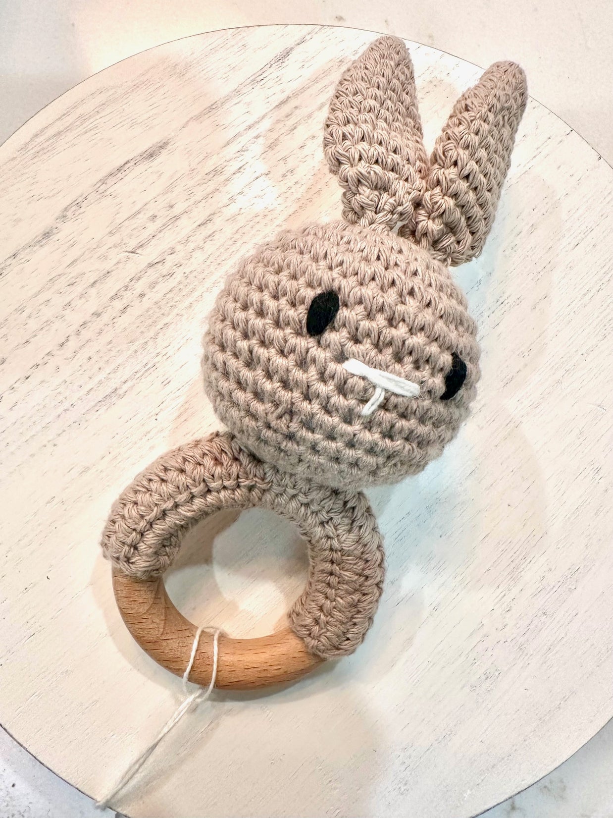 Crocheted beige bunny teething ring with natural wood circle base, black embroidered eyes and white cotton tail detail