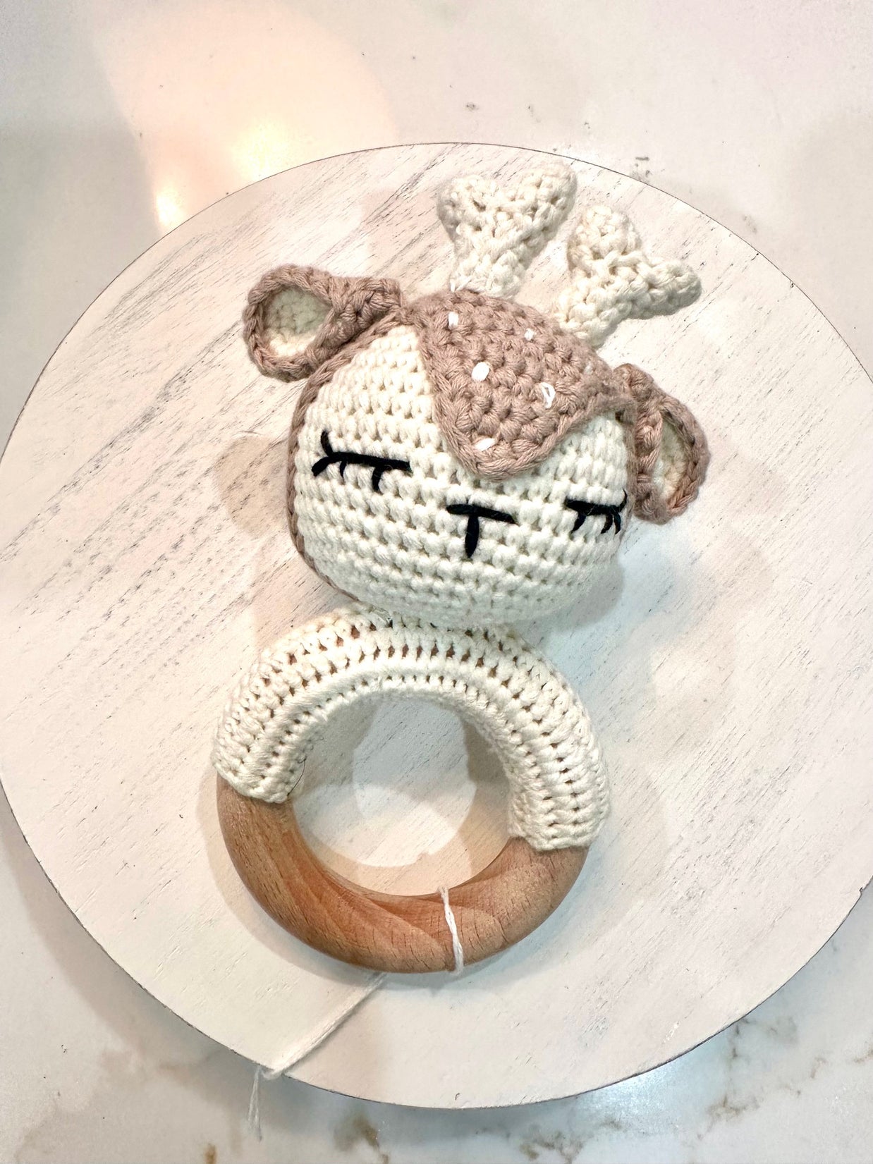 Crocheted bunny baby rattle in cream and taupe yarn with embroidered sleepy eyes attached to wooden teething ring