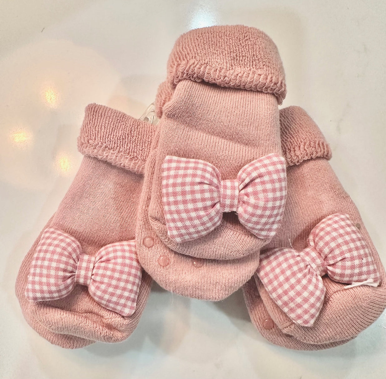 Dusty pink knit baby socks with pink and white gingham bows on top and textured non-slip grips on soles