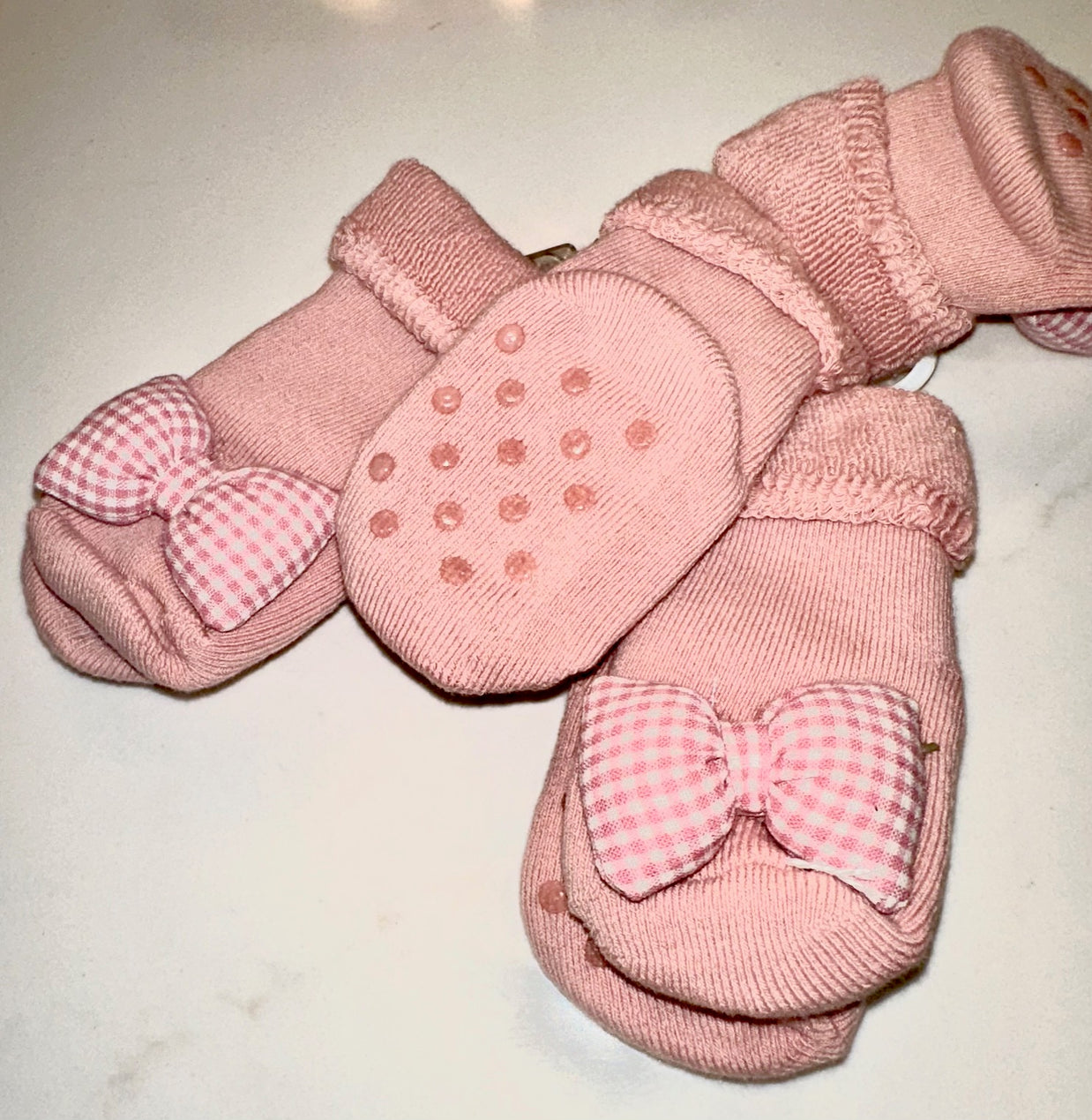 Dusty pink knit baby mittens with non-slip dots and pink gingham bow accents on neutral background