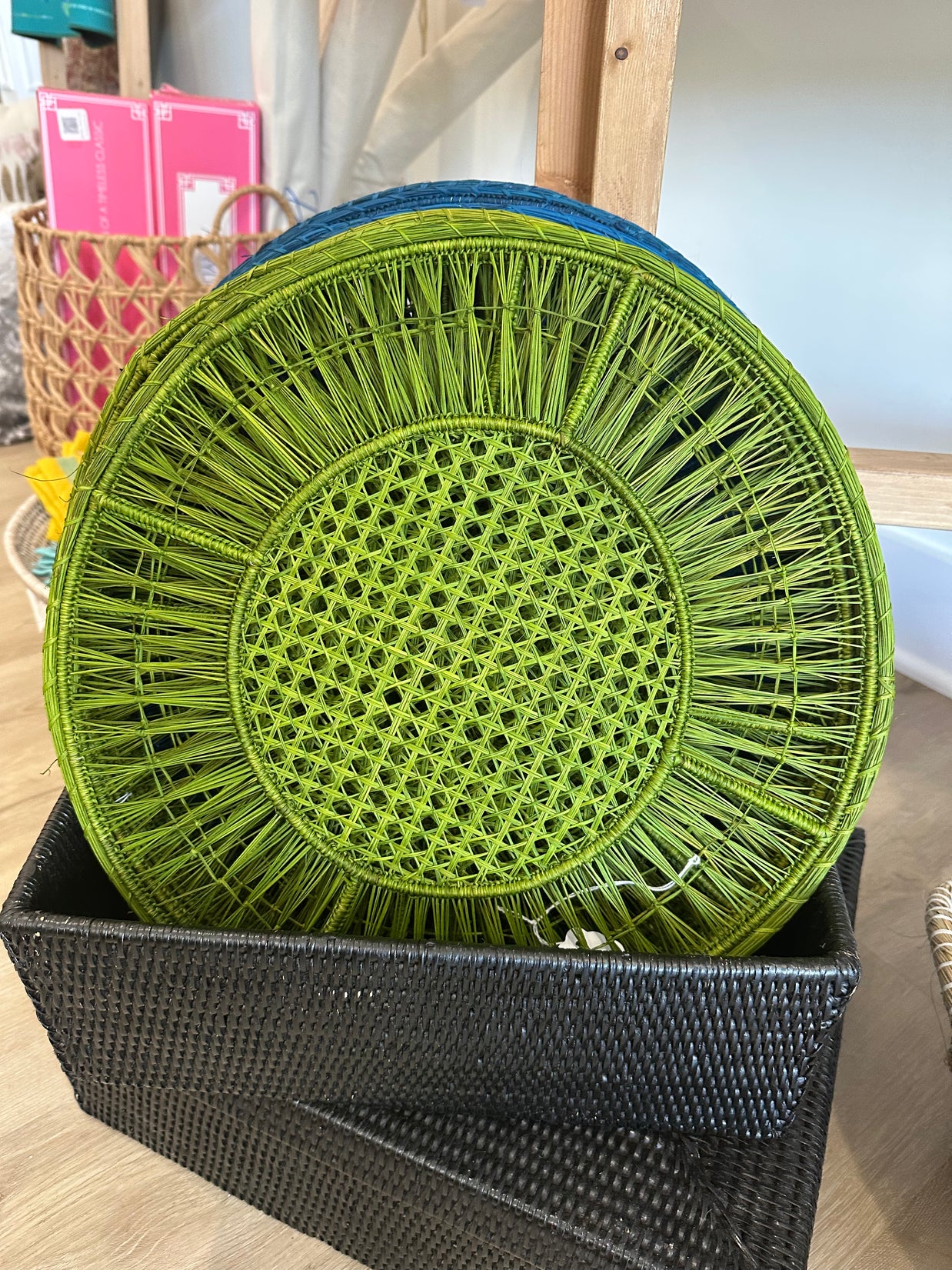 Lime green woven rattan circular tray with teal rim and radiating spoke pattern on black woven storage box