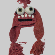 Hand-crocheted monster winter hat in dusty rose yarn with bulging white eyes, white teeth, braided earflaps and tassel trim