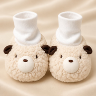 Pair of plush animal slippers with face designs on a light surface.