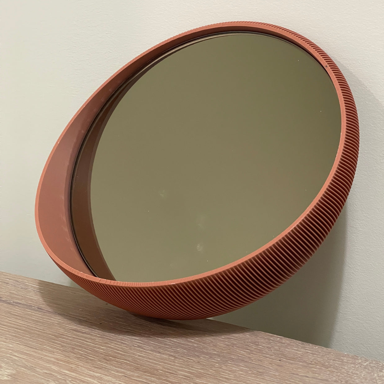 Round wall mirror with terracotta orange frame featuring fine ribbed texture detail and thick beveled edge on beige wall