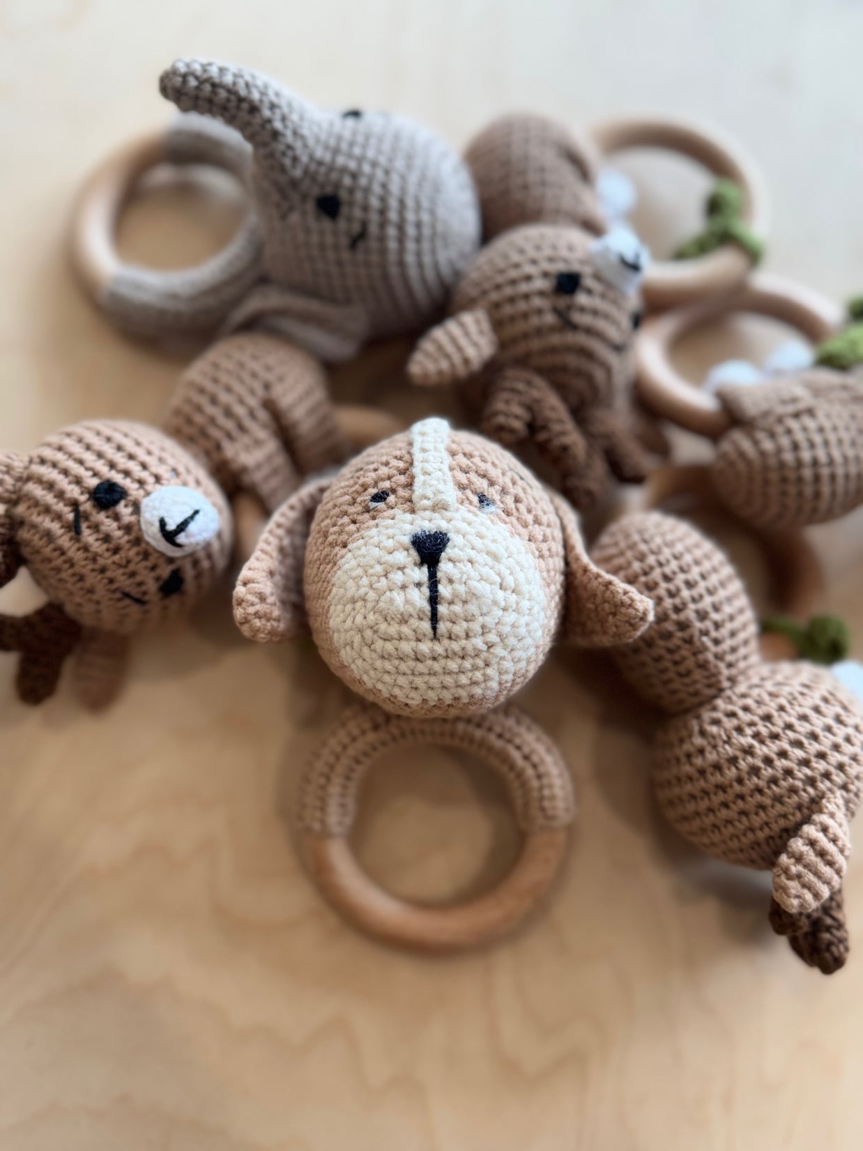 Handmade crochet baby toys in tan and cream yarn including rattles with wooden teething rings and plush animals