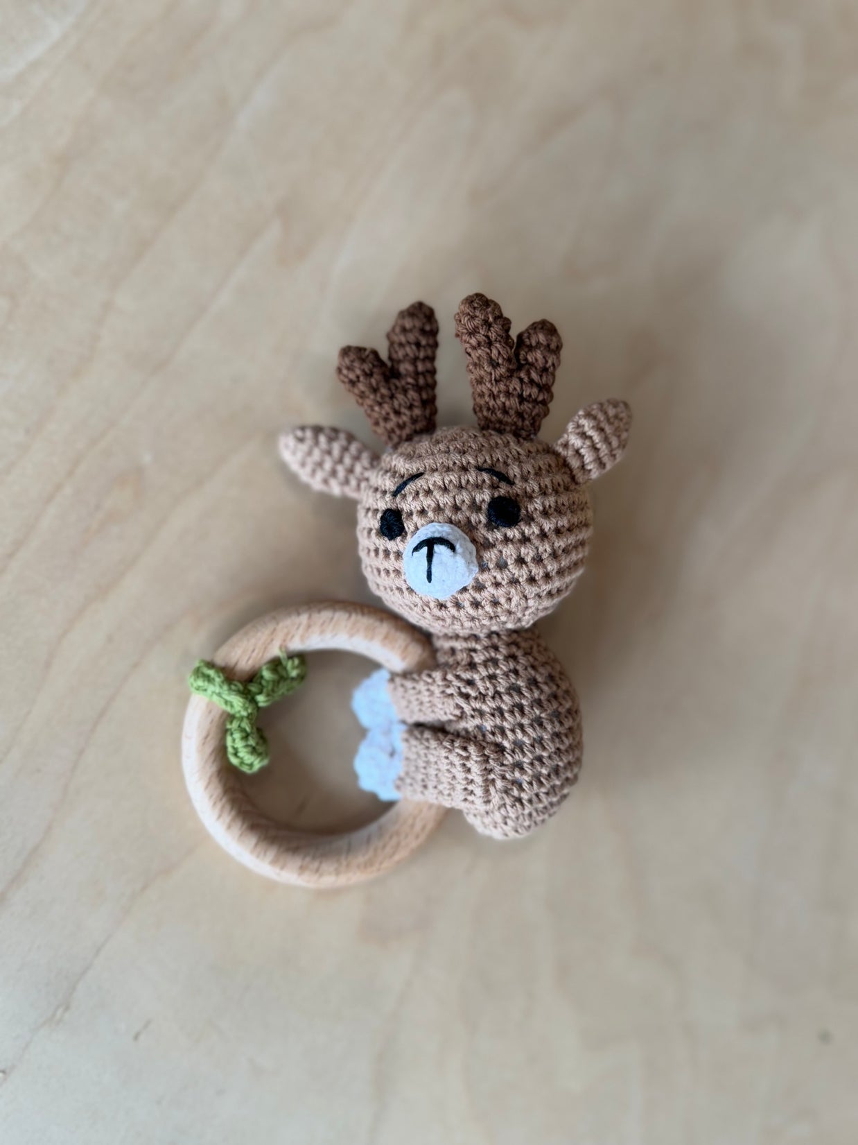 Crocheted beige reindeer baby rattle with brown antlers, light blue nose, natural wood teething ring with green bow accent