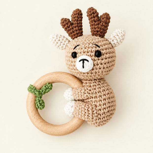 Crocheted beige reindeer baby rattle with brown antlers, light blue nose, natural wood teething ring with green bow accent