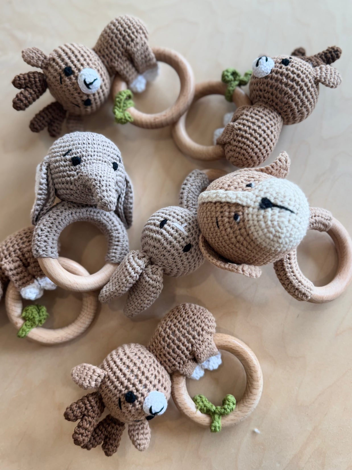 Handmade crocheted animal baby rattles with wooden teething rings in beige and brown featuring deer, bunny, monkey, and sloth designs
