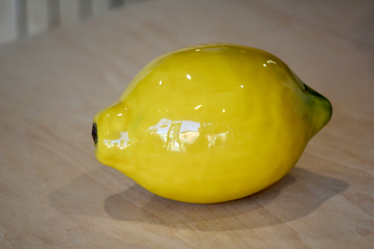 Glossy ceramic lemon-shaped bowl in bright yellow glaze with green leaf accent and textured stem detail on wood surface