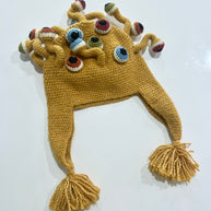 Mustard yellow crocheted monster hat with multiple eyeball tentacles in blue, green, and burgundy, braided ear flaps with tassels