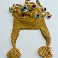 Mustard yellow crocheted winter hat with ear flaps, yarn tassels, and multiple colorful eyeball tentacles on top