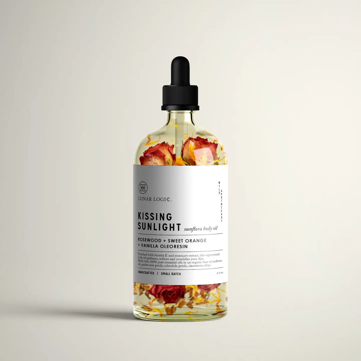 Clear glass dropper bottle with dried rose petals and calendula suspended in golden oil, white minimal label, black cap