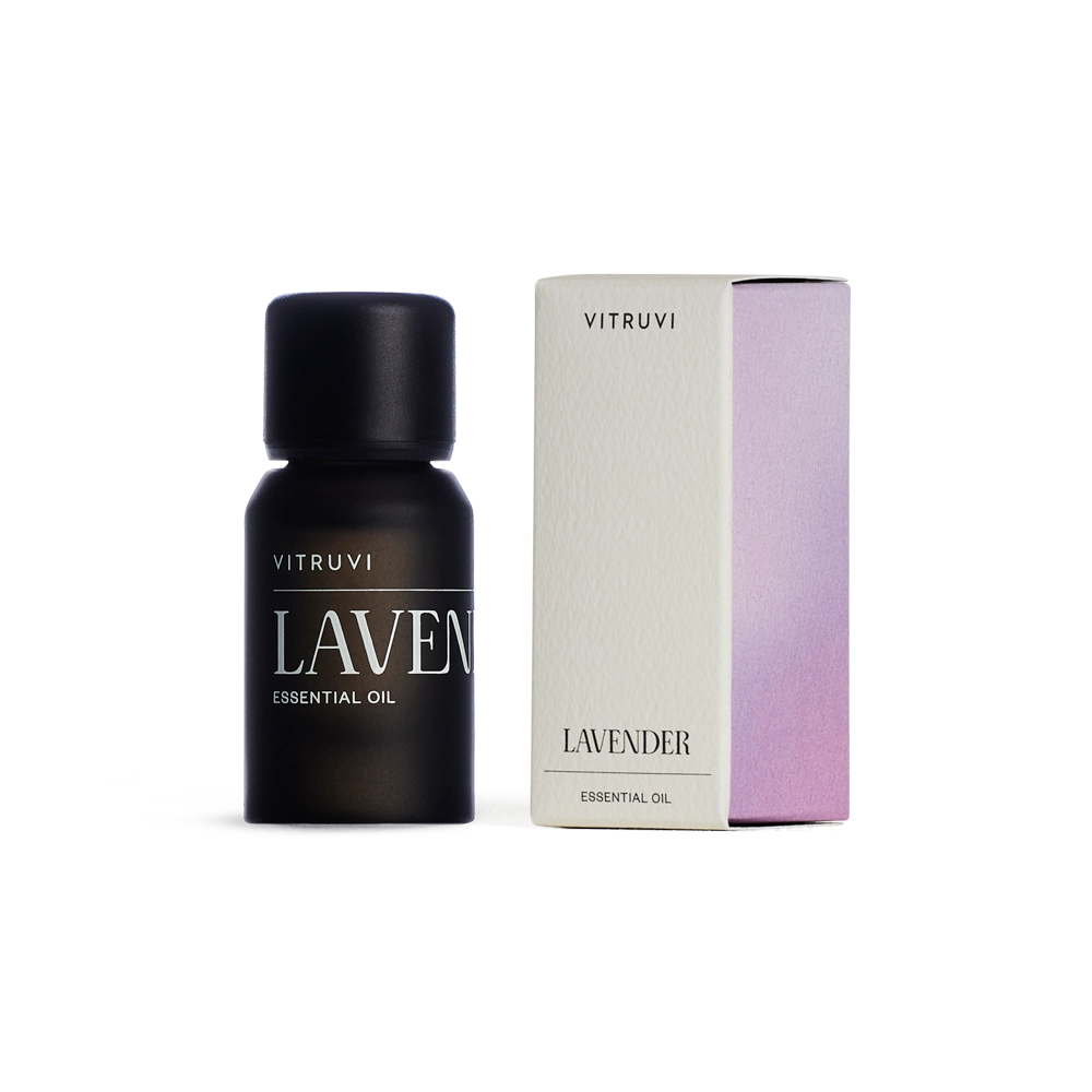 Matte black glass bottle of Vitruvi lavender essential oil beside cream and lilac rectangular packaging box on white background