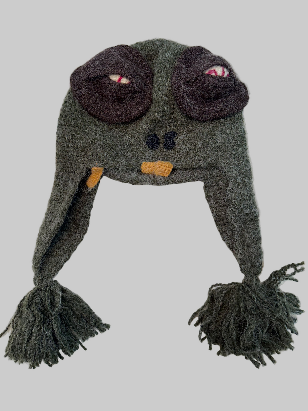 Gray knit monster aviator hat with brown goggle detail, orange bow tie, braided ear flaps with yarn tassels