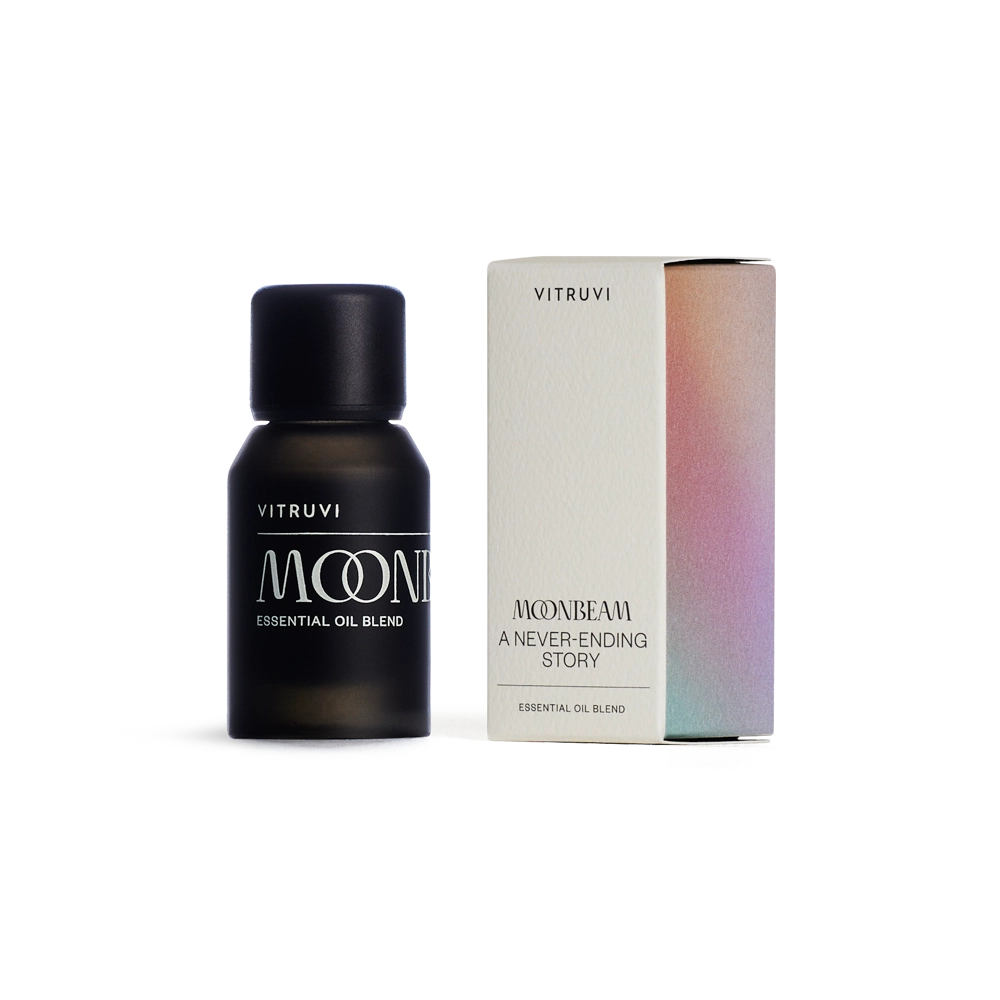 Matte black bottle of Vitruvi Moonbeam essential oil blend beside gradient holographic box in peach, pink and turquoise tones