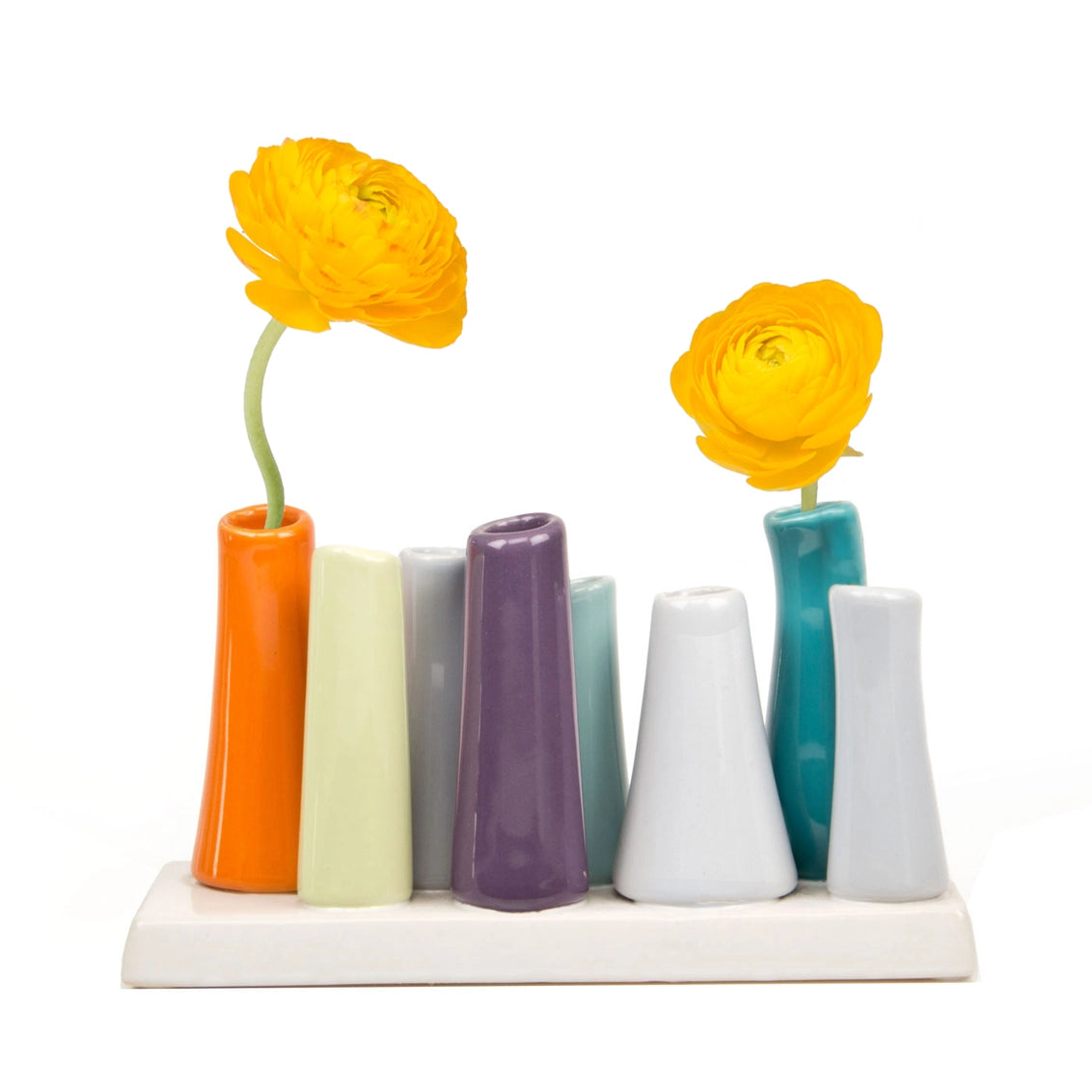 Multi-tube ceramic bud vase set with glossy orange, mint, gray, purple, white, and teal cylinders holding yellow ranunculus flowers