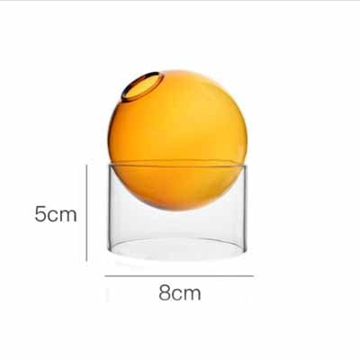 Bright orange spherical container with dark circular opening on top, suspended in clear cylindrical glass base with dimensions
