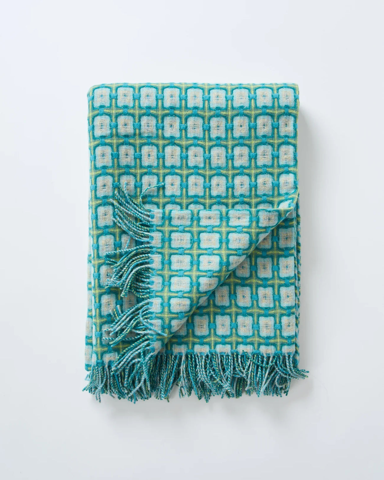 Woven throw blanket with turquoise, cream and sage geometric tile pattern and knotted fringe trim folded on white surface