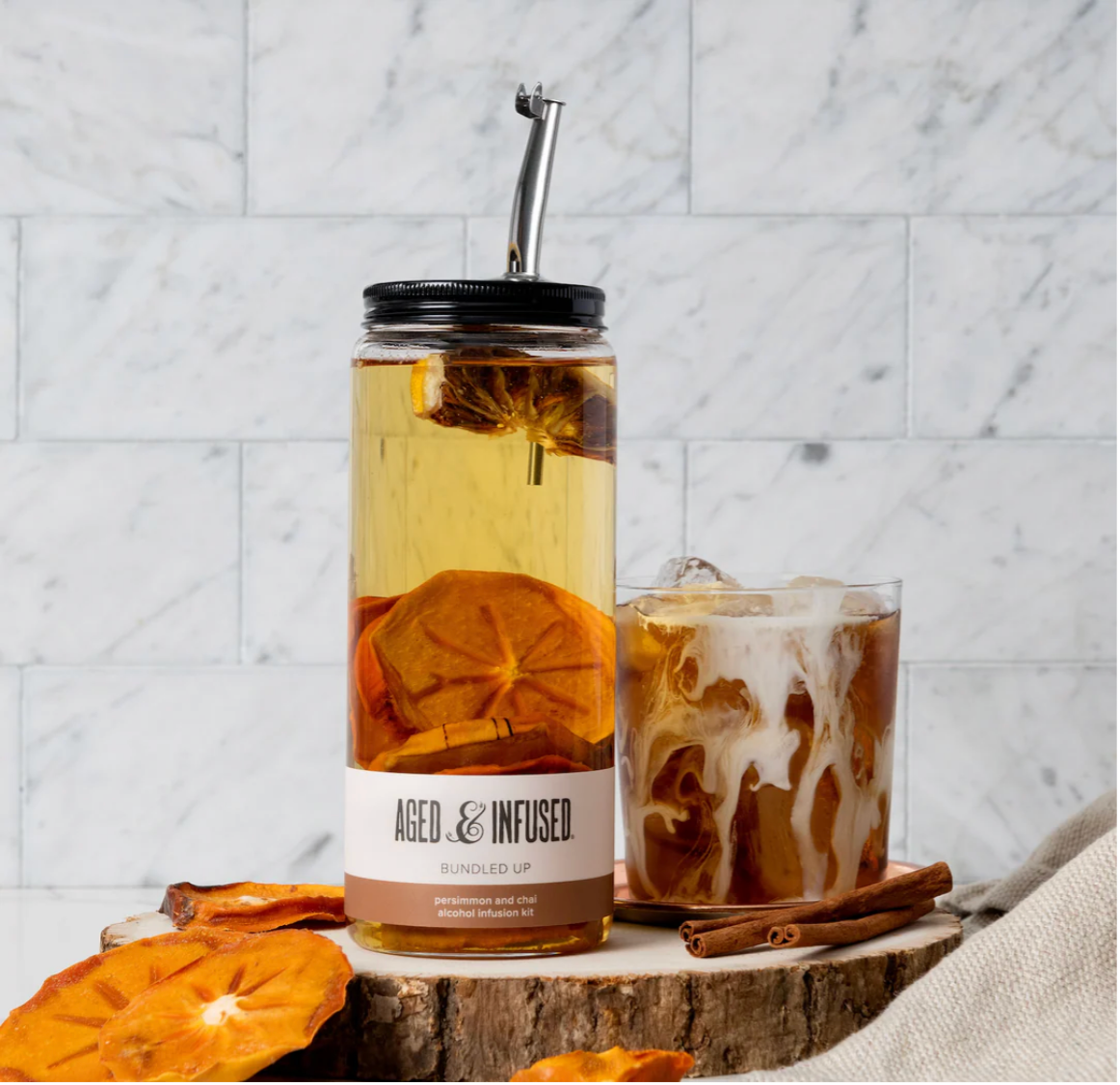 Glass mason jar infusion kit with dried orange slices and cinnamon sticks in amber liquid with metal straw and black lid