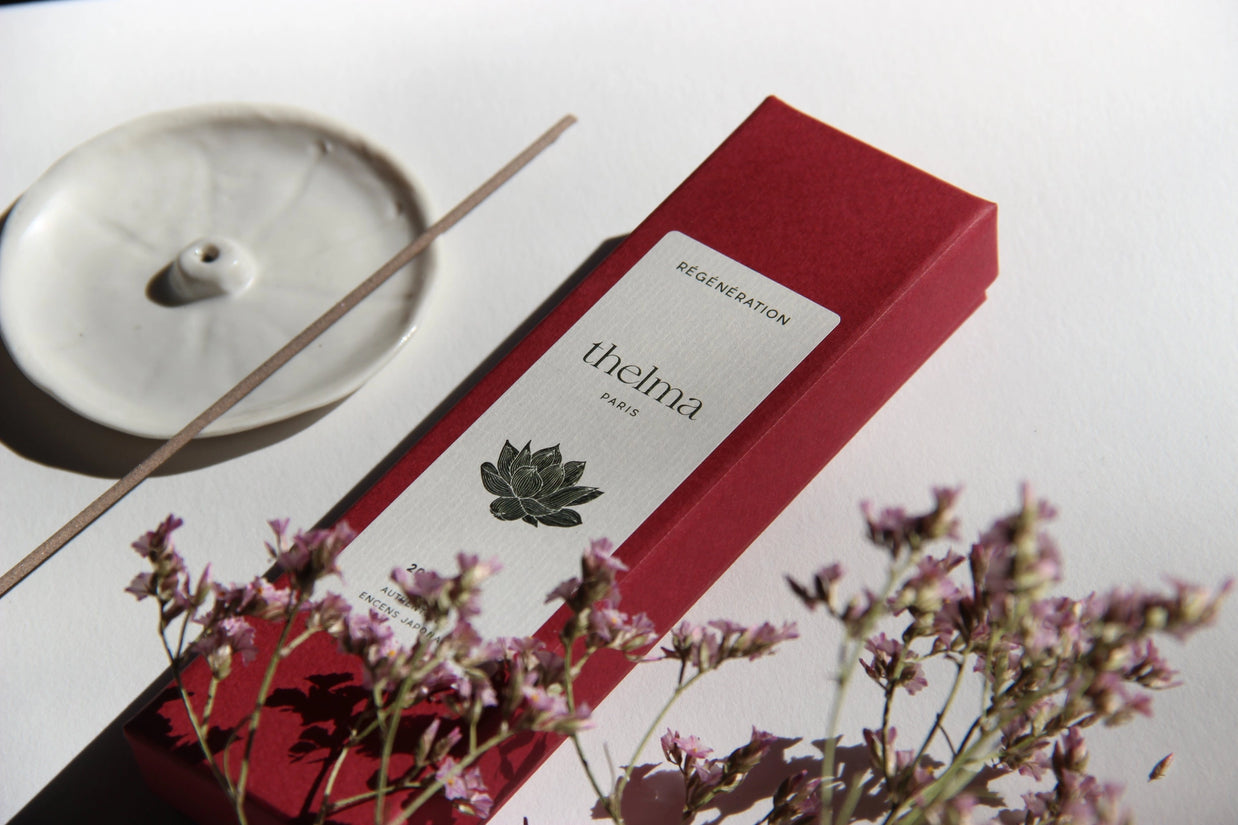 Deep red incense box labeled thelma Paris with lotus illustration beside ceramic holder and dried purple flowers