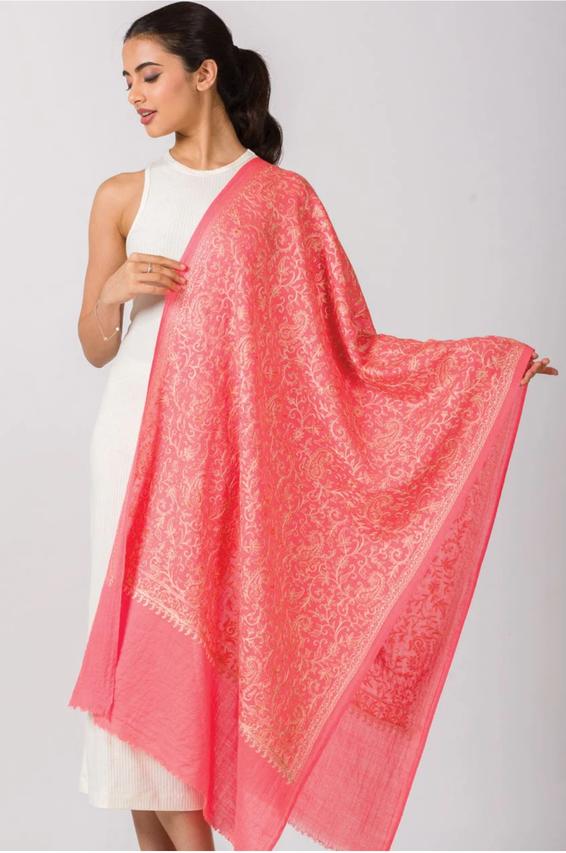 Coral pink pashmina shawl with gold metallic paisley embroidery and frayed edges draped over white sleeveless dress