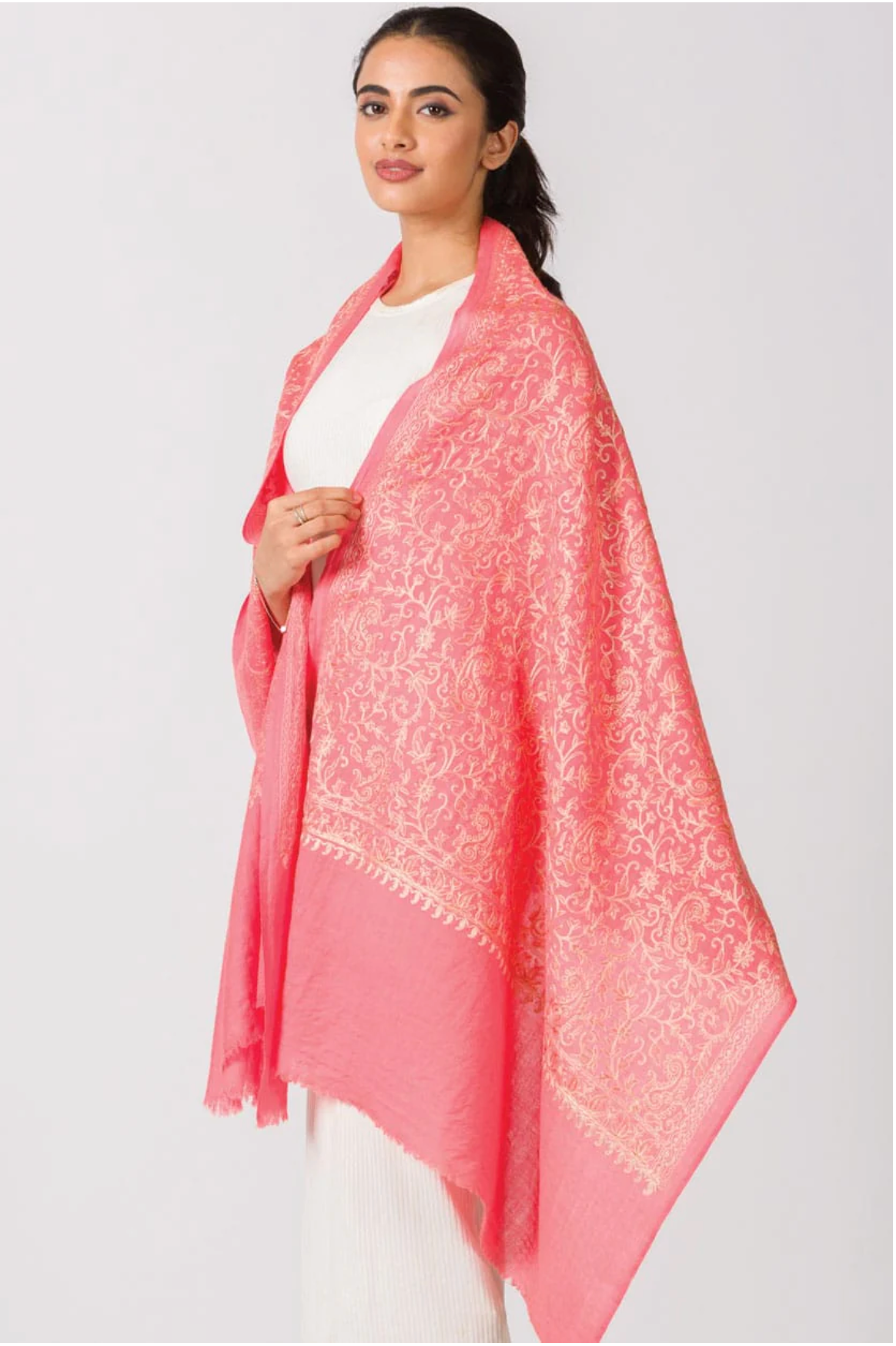 Coral pink pashmina shawl with intricate cream paisley embroidery and frayed edges draped over white outfit