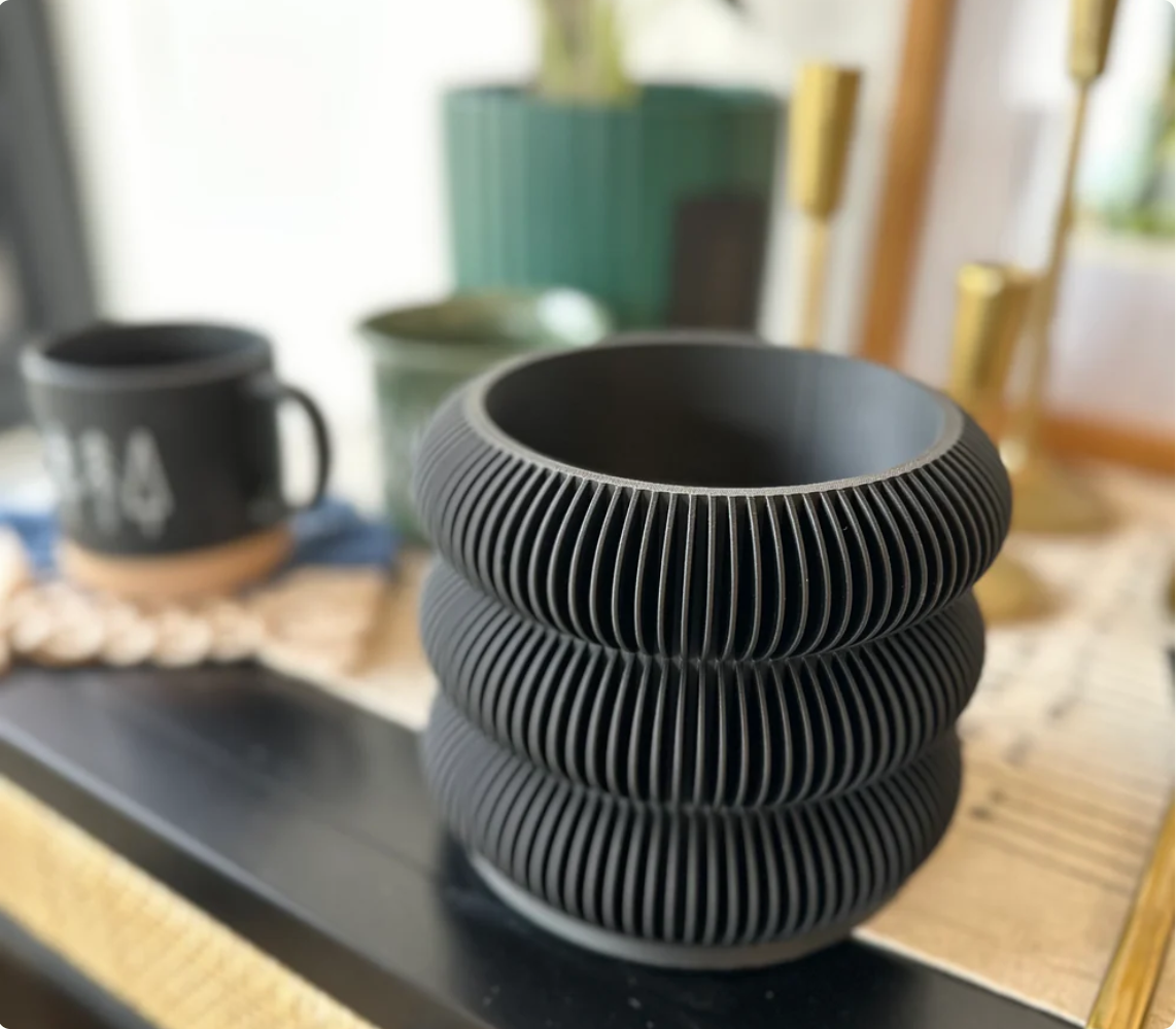 Matte black ceramic planter with three stacked ribbed bands creating modern accordion-style texture on rounded vessel