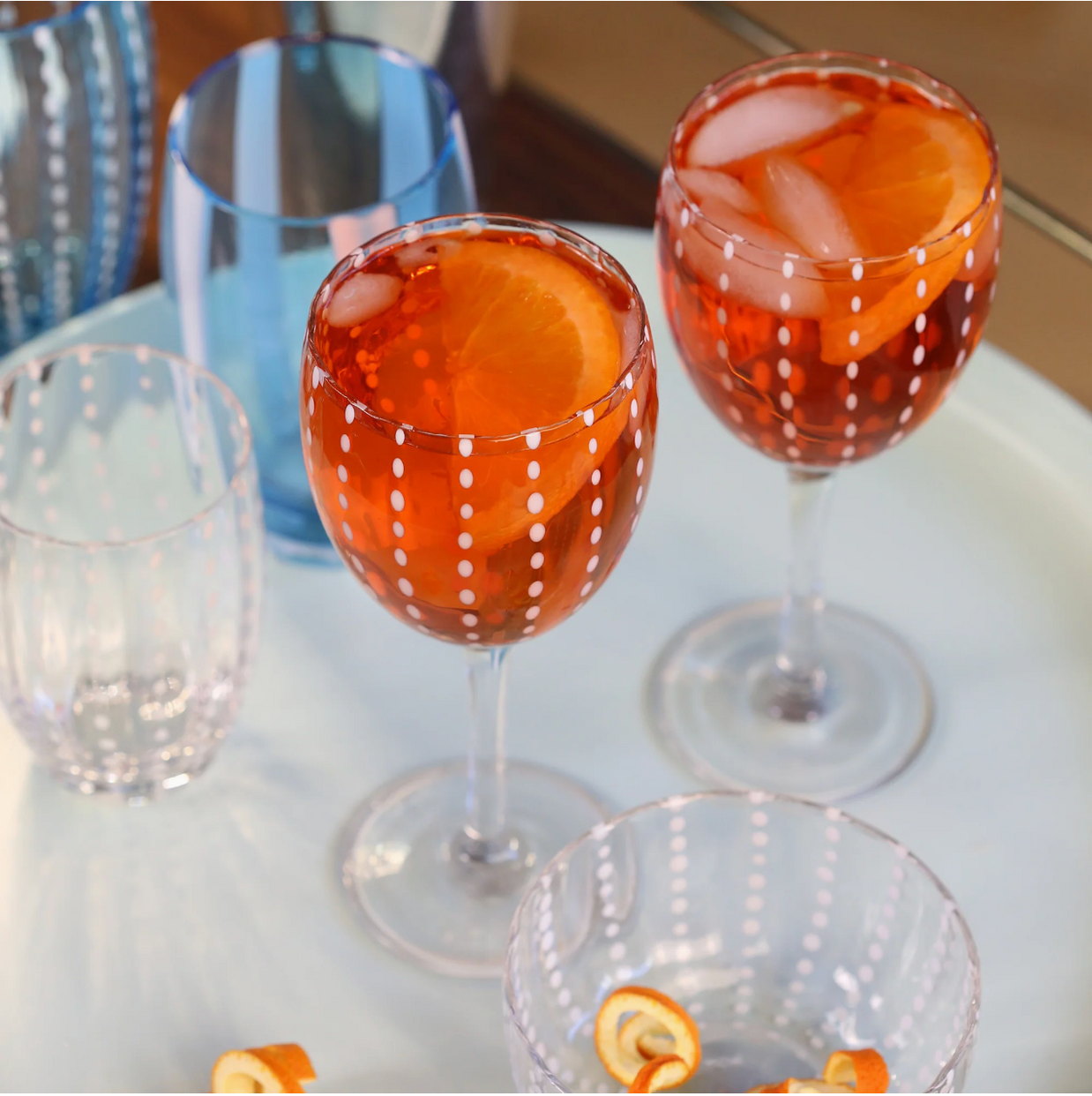 Orange cocktails in white dotted stemmed wine glasses with coordinating blue striped glassware on white surface
